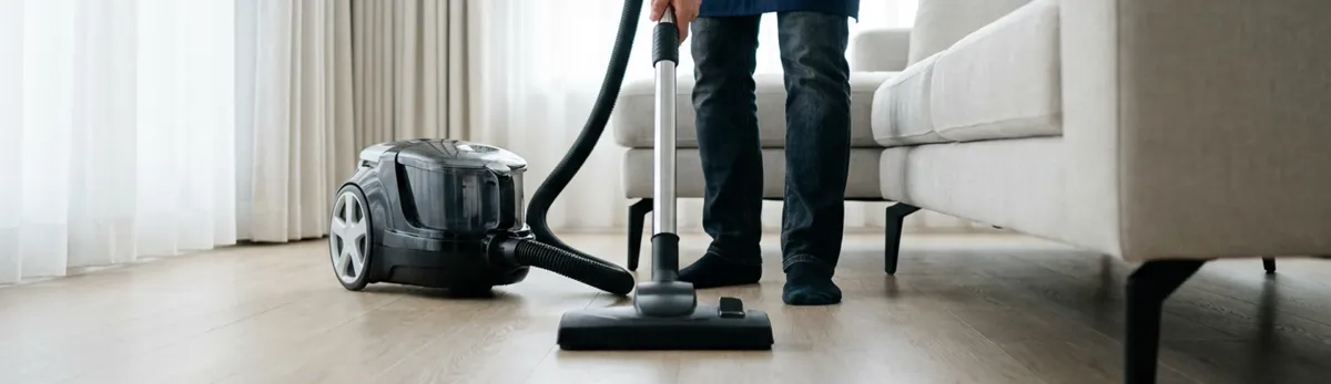 Professional house cleaner vacuuming a living room floor with a canister vacuum cleaner, Gilbert, AZ.